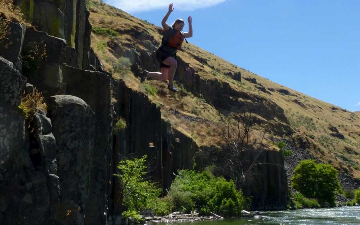 a person wearing a life jacket is in mid-air after jumping off a rock face into the water